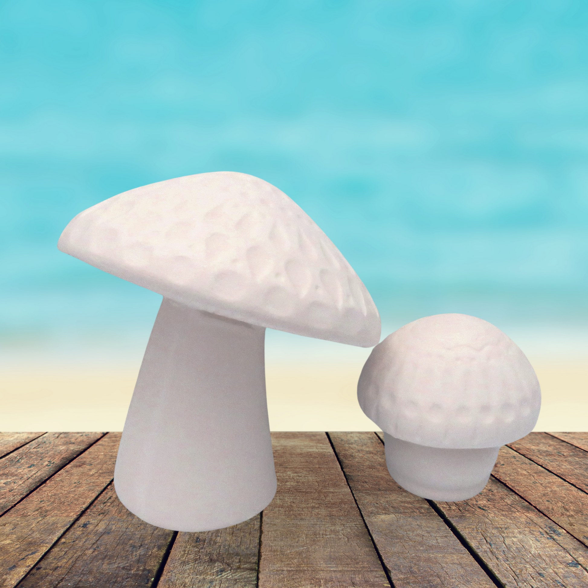 Set of 2 handmade ready to paint ceramic mushrooms figurines on a rustic wood table by the ocean.