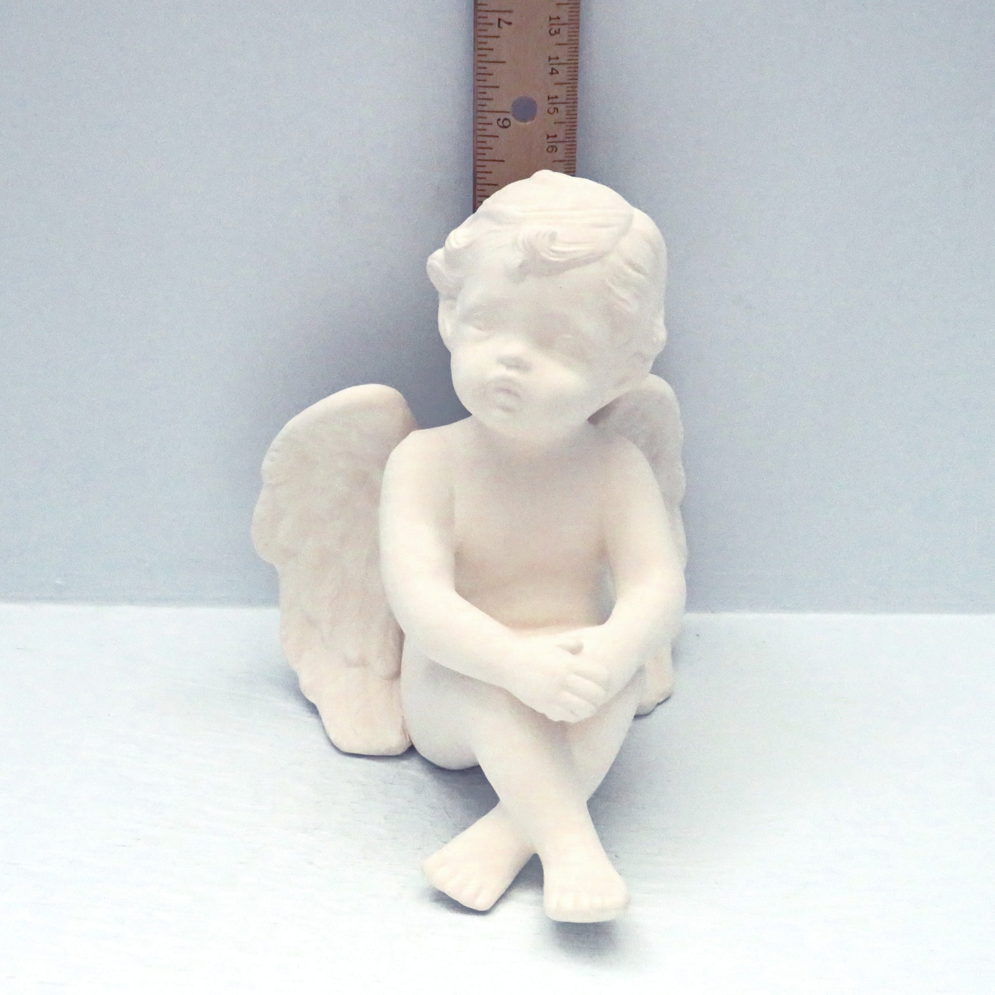 Ceramic cherub to paint sitting in front of a ruler showing it to be approximately 5 1/2 inches tall