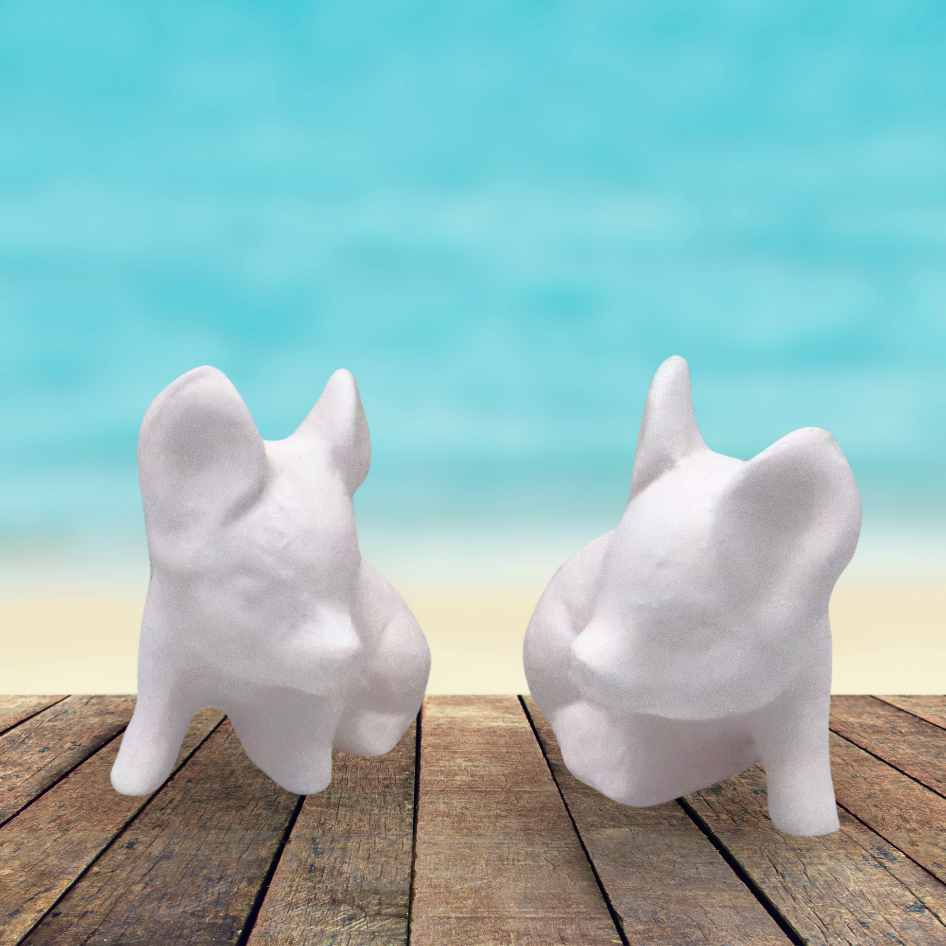 2 little unpainted ceramic pig figurines sitting on a rustic wooden table by the beach.