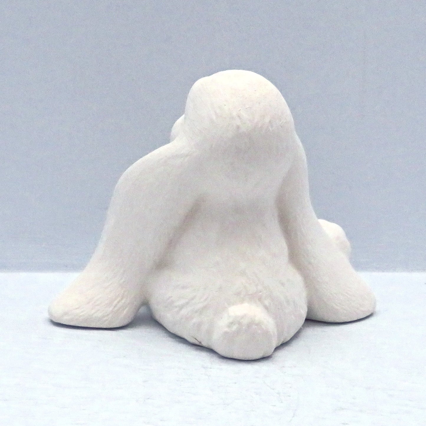 Back view of ready to paint lop eared bunny showing round tail, long ears sitting on a pale blue background.