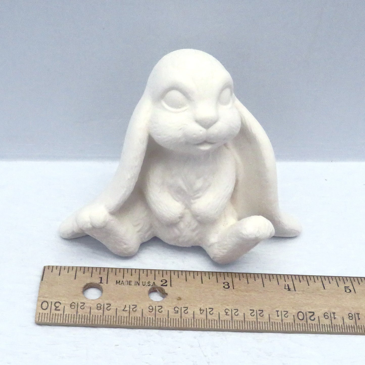 View looking down on unpainted bisque lop eared bunny near  ruler showing it to be approximately 4 1/8 inches wide