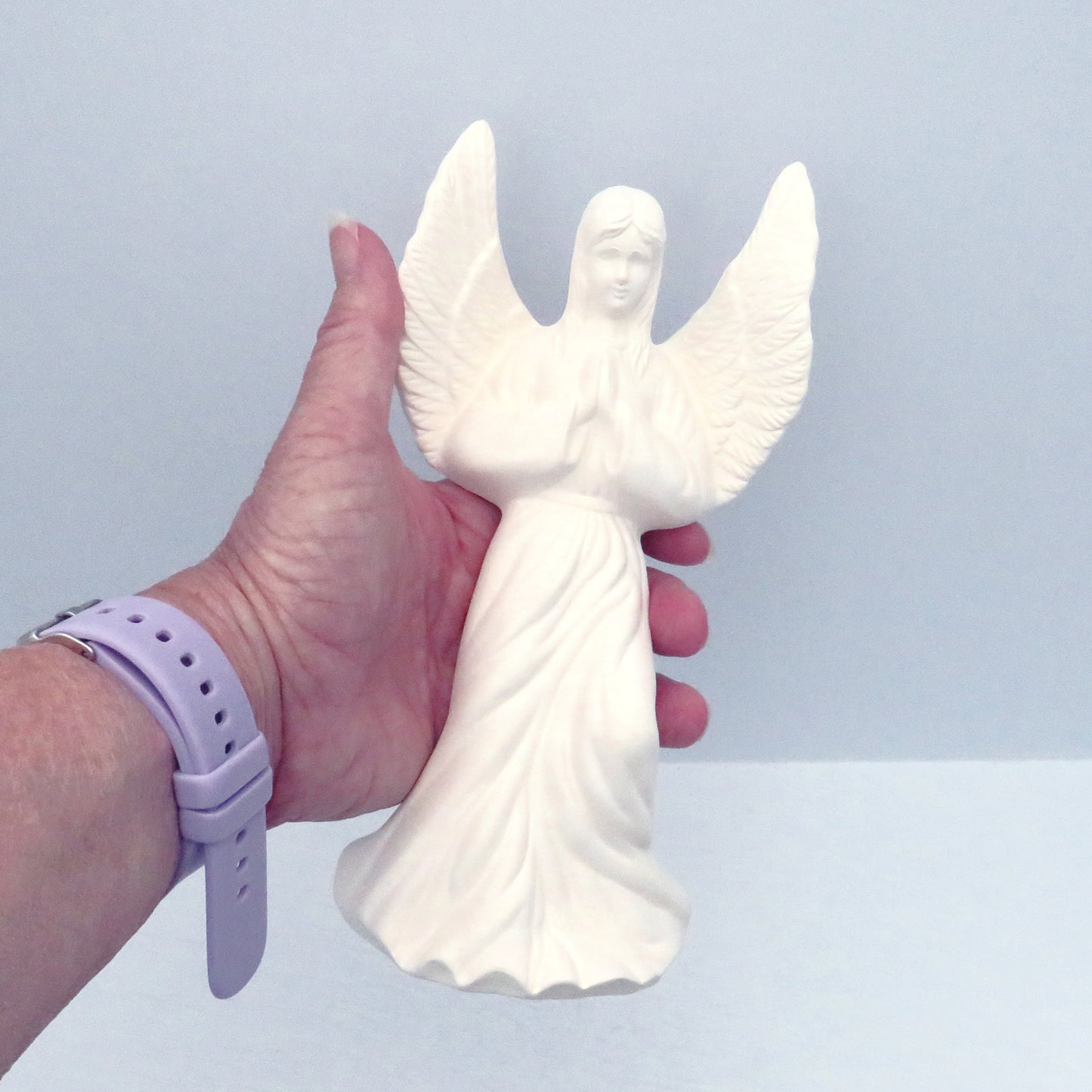 Ready to paint praying ceramic angel figurine in my hand showing her face, hair, praying hands, wings, and dress.  This also shows that she fits in my hand.