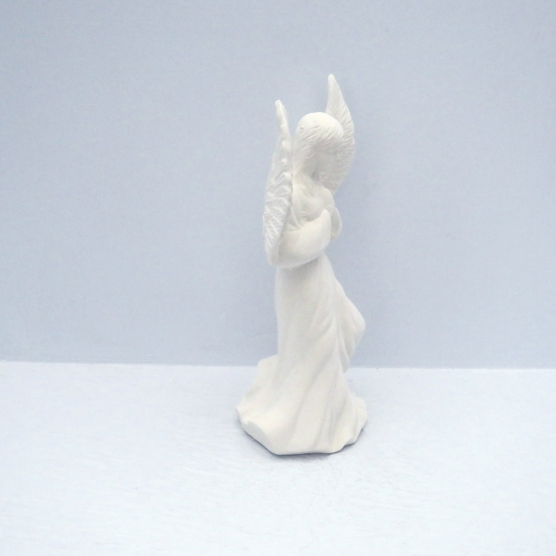 side view of white bisque ready to paint praying ceramic angel with wings outstretched.