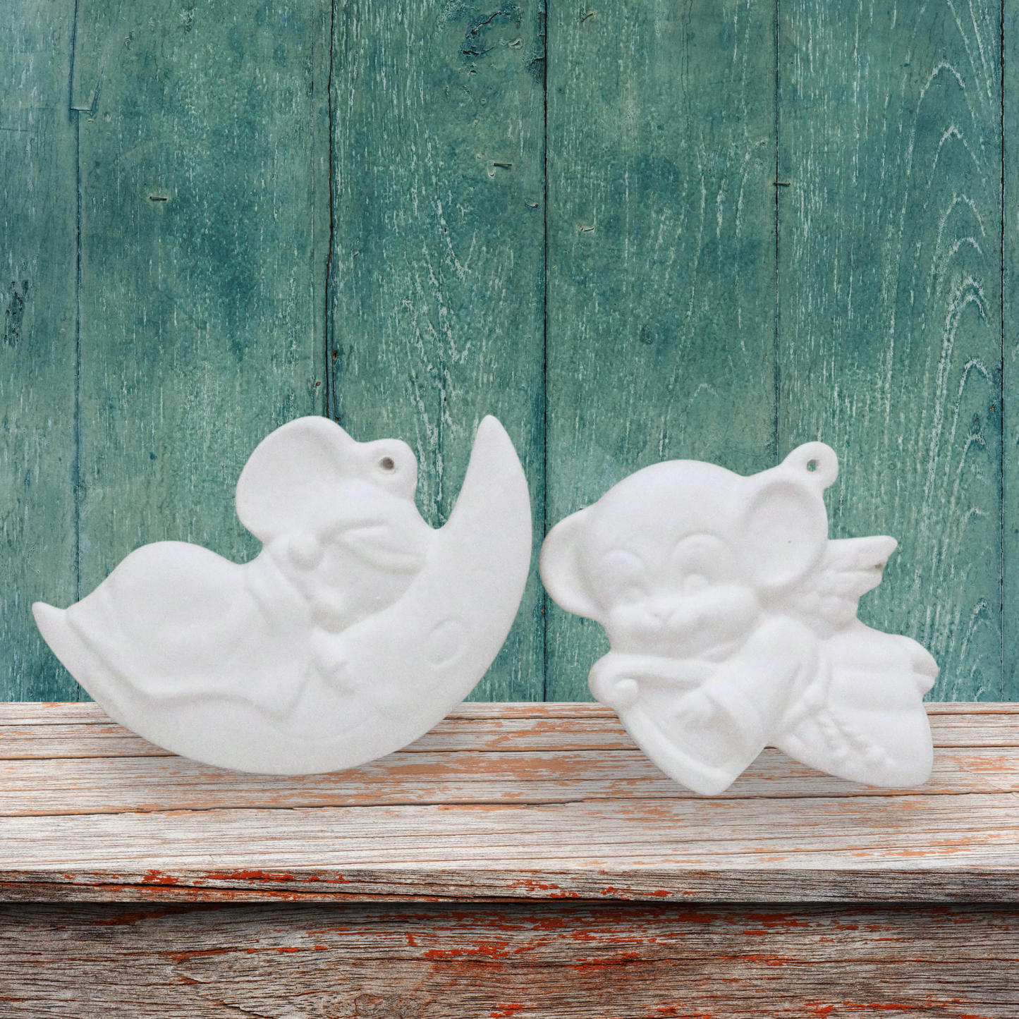 2 ready to paint ceramic Christmas Tree ornaments.  One is a mouse asleep on a moon, one is an angel mouse with a harp.  They are on a shelf with a green background