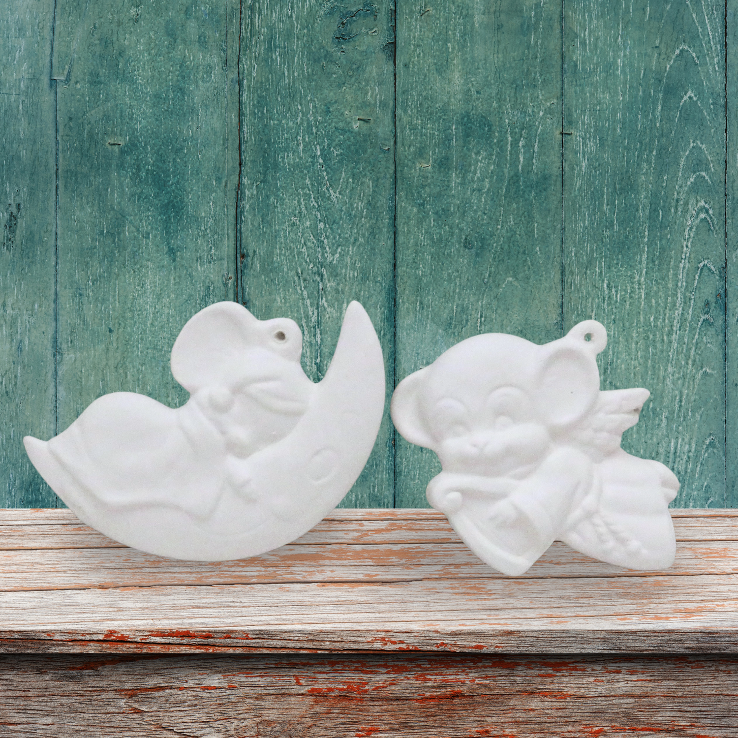 2 ready to paint ceramic Christmas Tree ornaments.  One is a mouse asleep on a moon, one is an angel mouse with a harp.  They are on a shelf with a green background