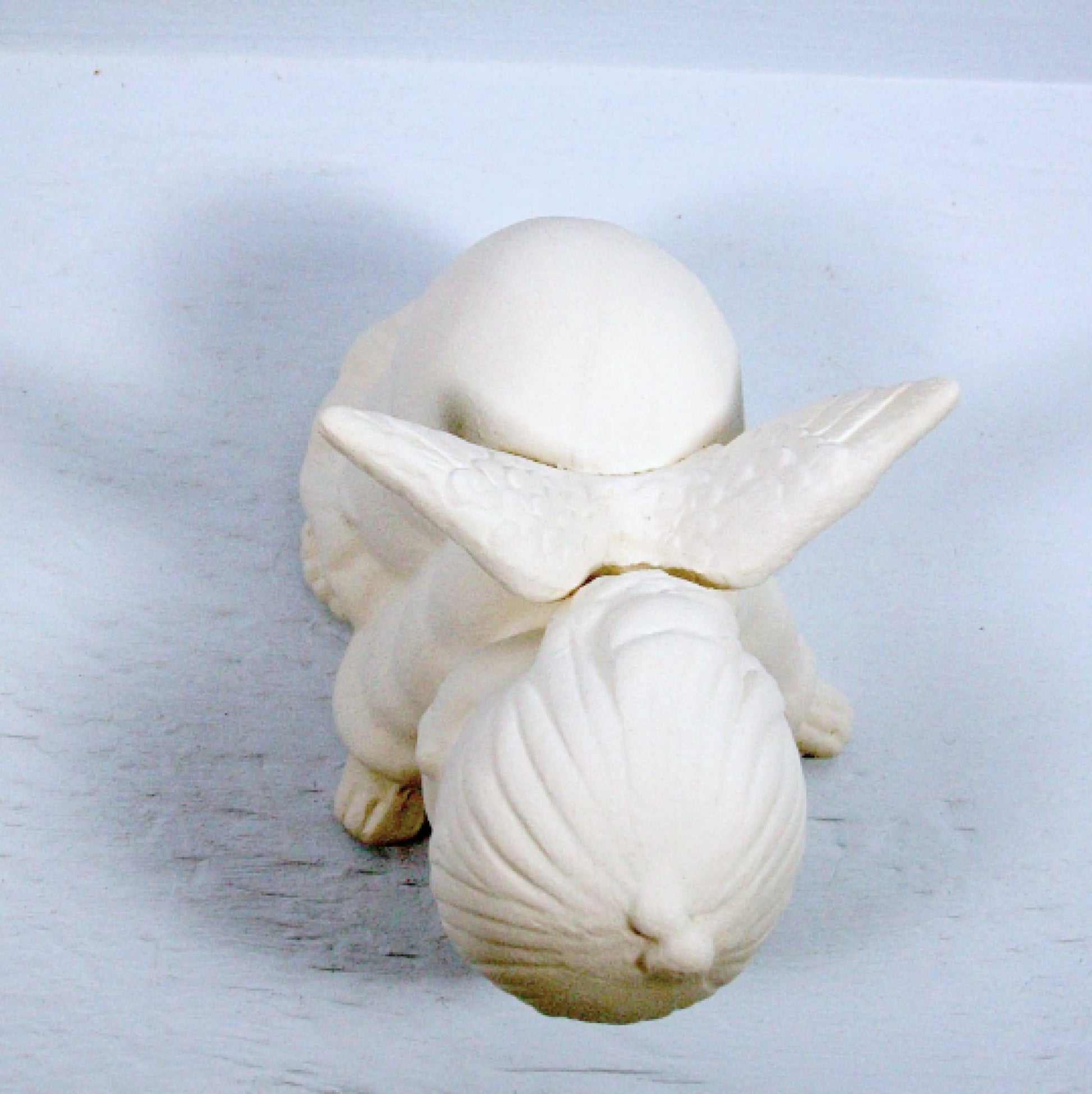 Top view of handmade unpainted ceramic angel statue showing wings open .  She is on a pale blue background