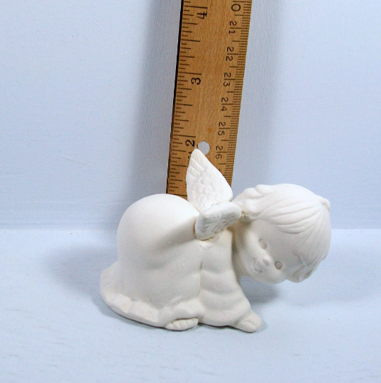 Handmade cute angel playing on all 4's with face toward camera.  She is near a ruler showing the statue to be approximately 2 inches tall at the tip of her wing.