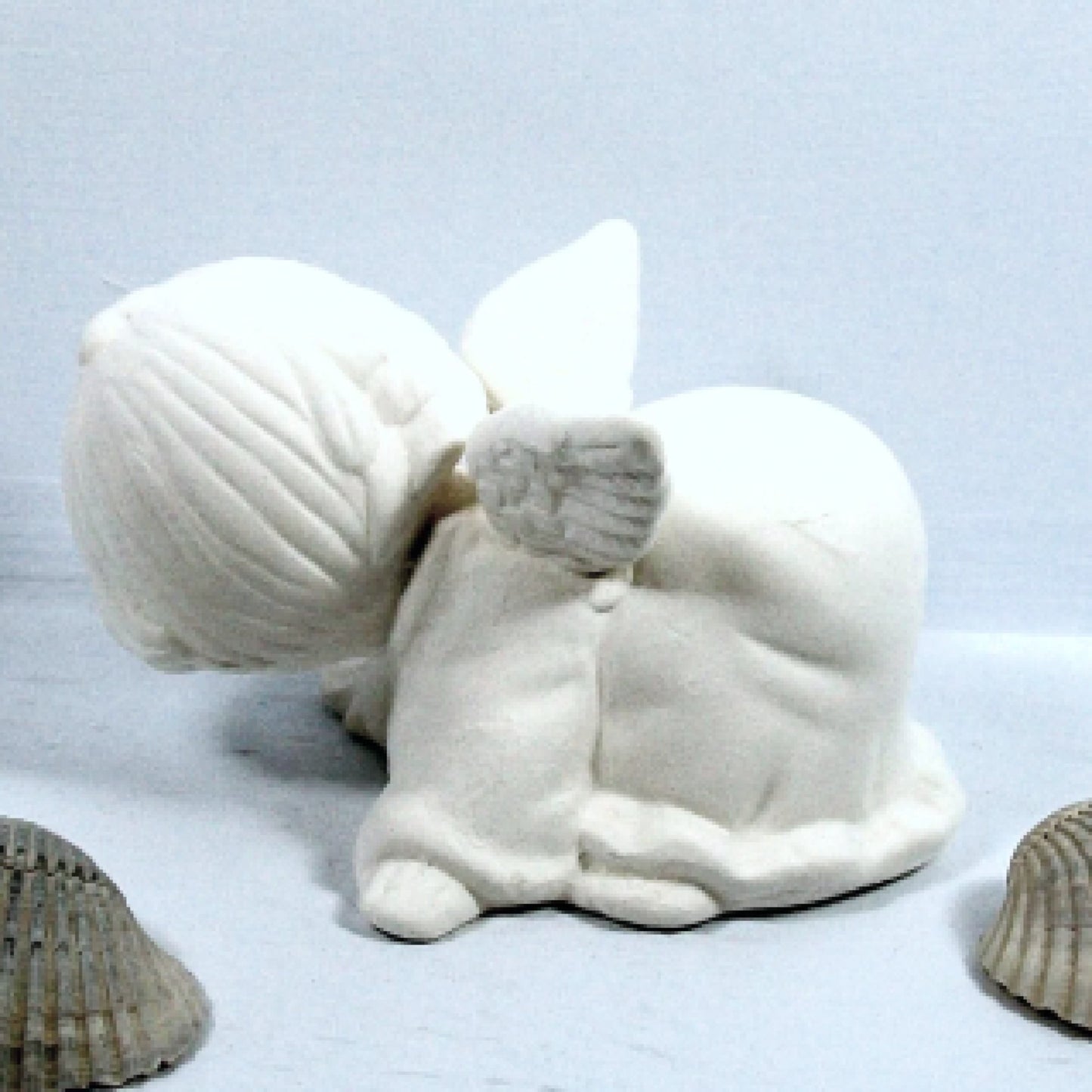Handmade Ready to paint ceramic playful angel figurine showing side and head turned away from the camera.