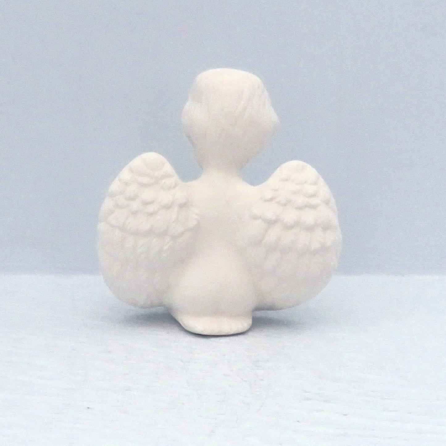 back view of a handmade paintable ceramic praying cherub on knees