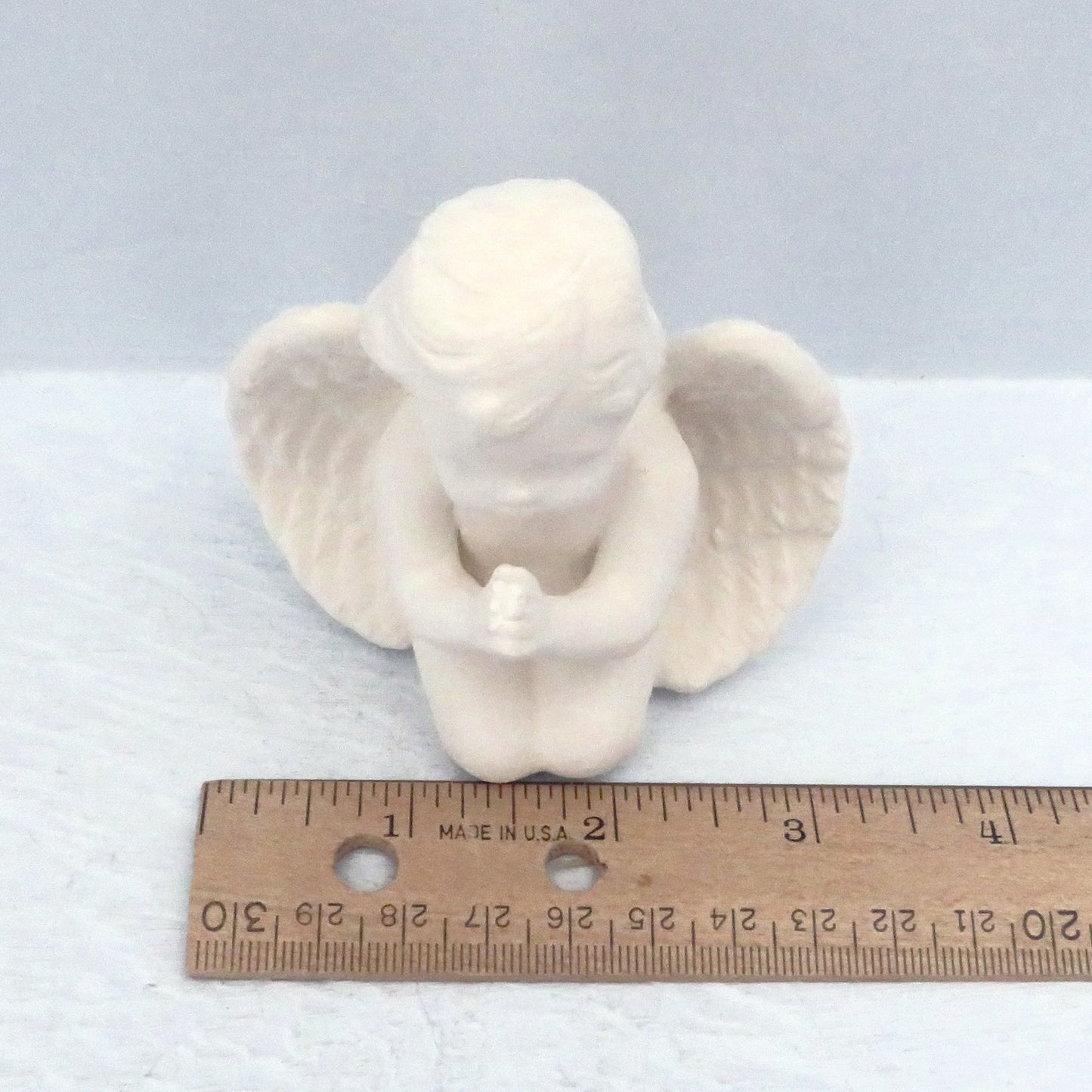Top view of white bisque paintable ceramic praying angel on knees showing it to be approximately 3 1/4 inche across