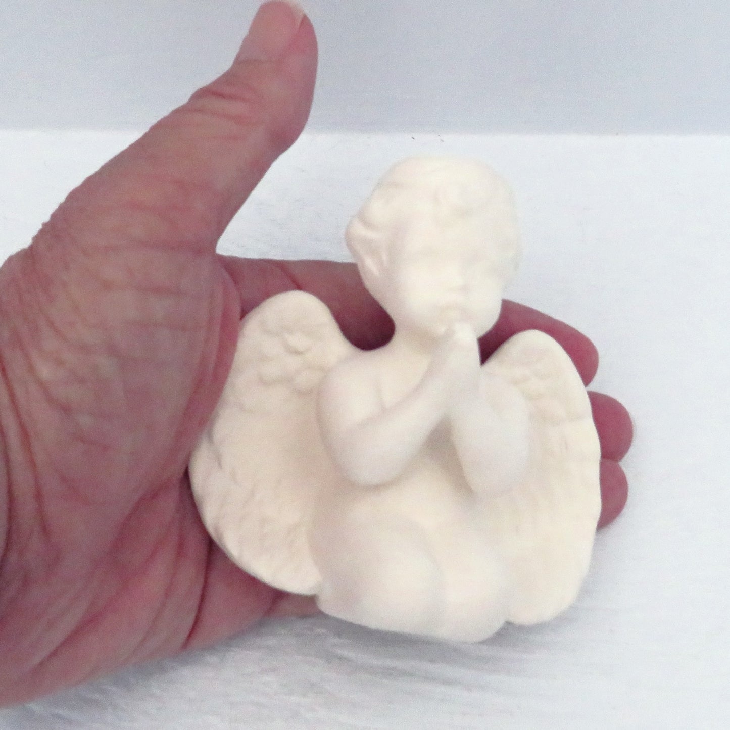 Unpainted ceramic cherub angel with hands folded in my hand showing size
