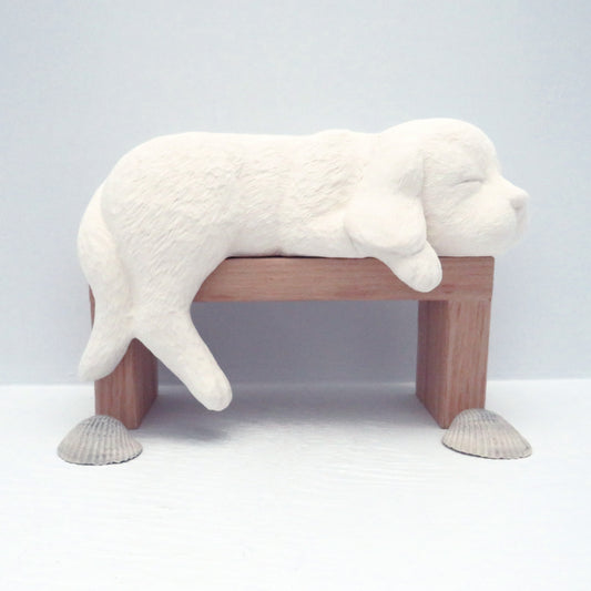 Ready to paint ceramic dog figurine on wood pedestal with sea shells on the pale blue table.  This is a side view of the dog