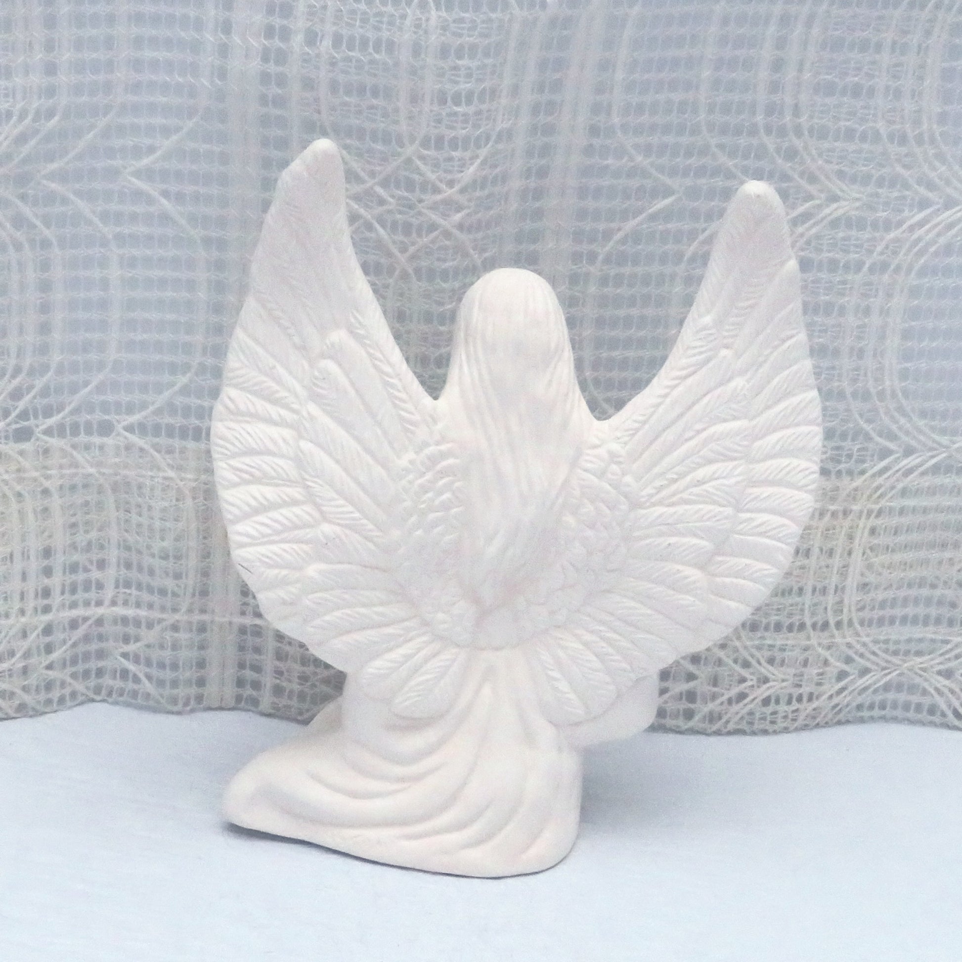 Rear view of unpainted ceramic angel figurine showing wings, long hair, and tunic.