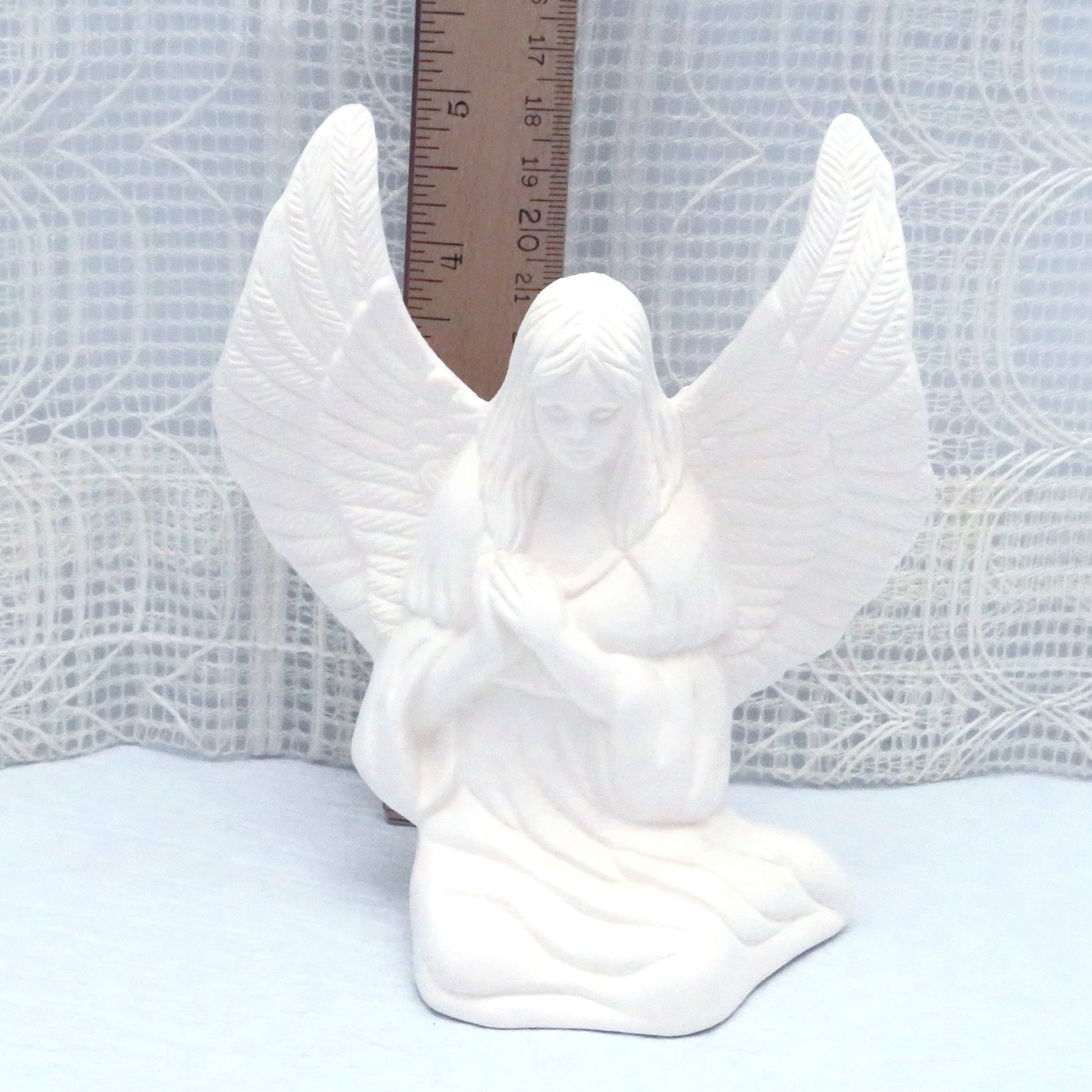 Ceramic angel to paint near a ruler showing her wing to be approximately 5 inches high.