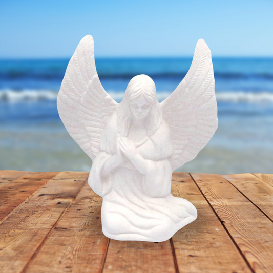 Handmade ready to paint ceramic angel figurine sitting on wood table near the ocean.