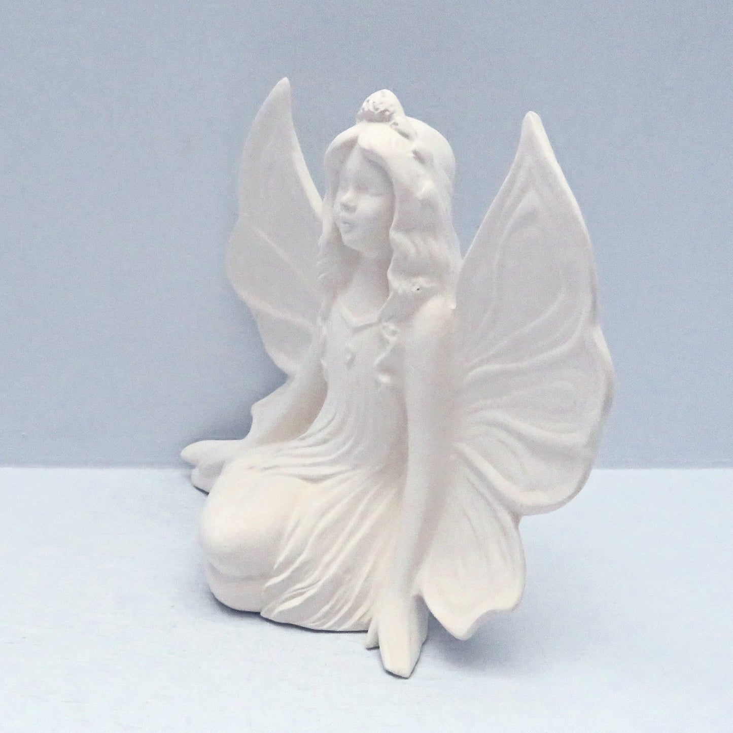 Side viwe of fairy statue, facing left, against a pale blue surface