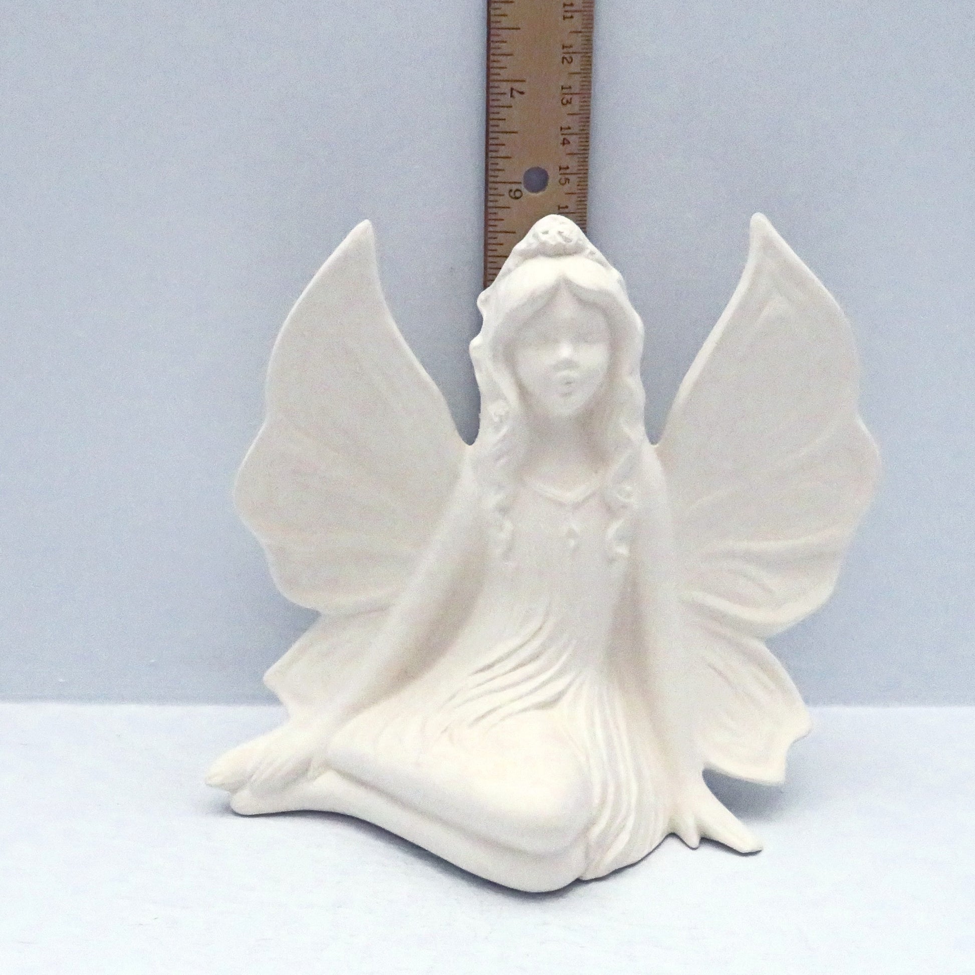 handmade ready to paint ceramic fairy figurine on a blue background with a ruler showing her to be almost 6 inches tall