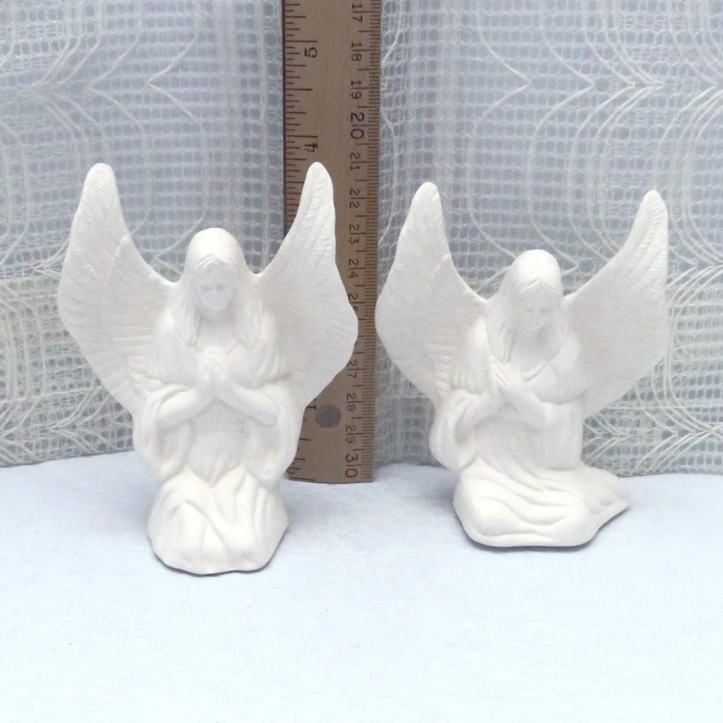 Handmade ceramic angels to paint in front of a ruler showing the tip of the wing to be almost 4 inches high.  The sitting angel is a bit shorter.