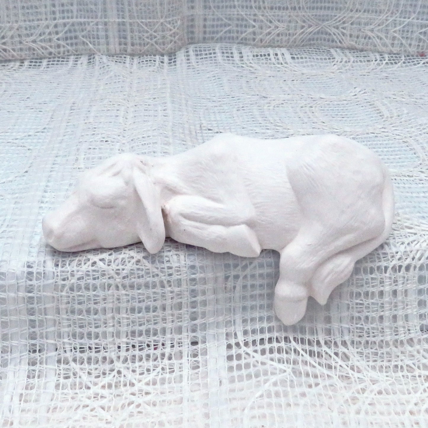 Handmade Ready to paint Ceramic shelf cow sitting on a lacy cloth with its left leg and tail hanging down