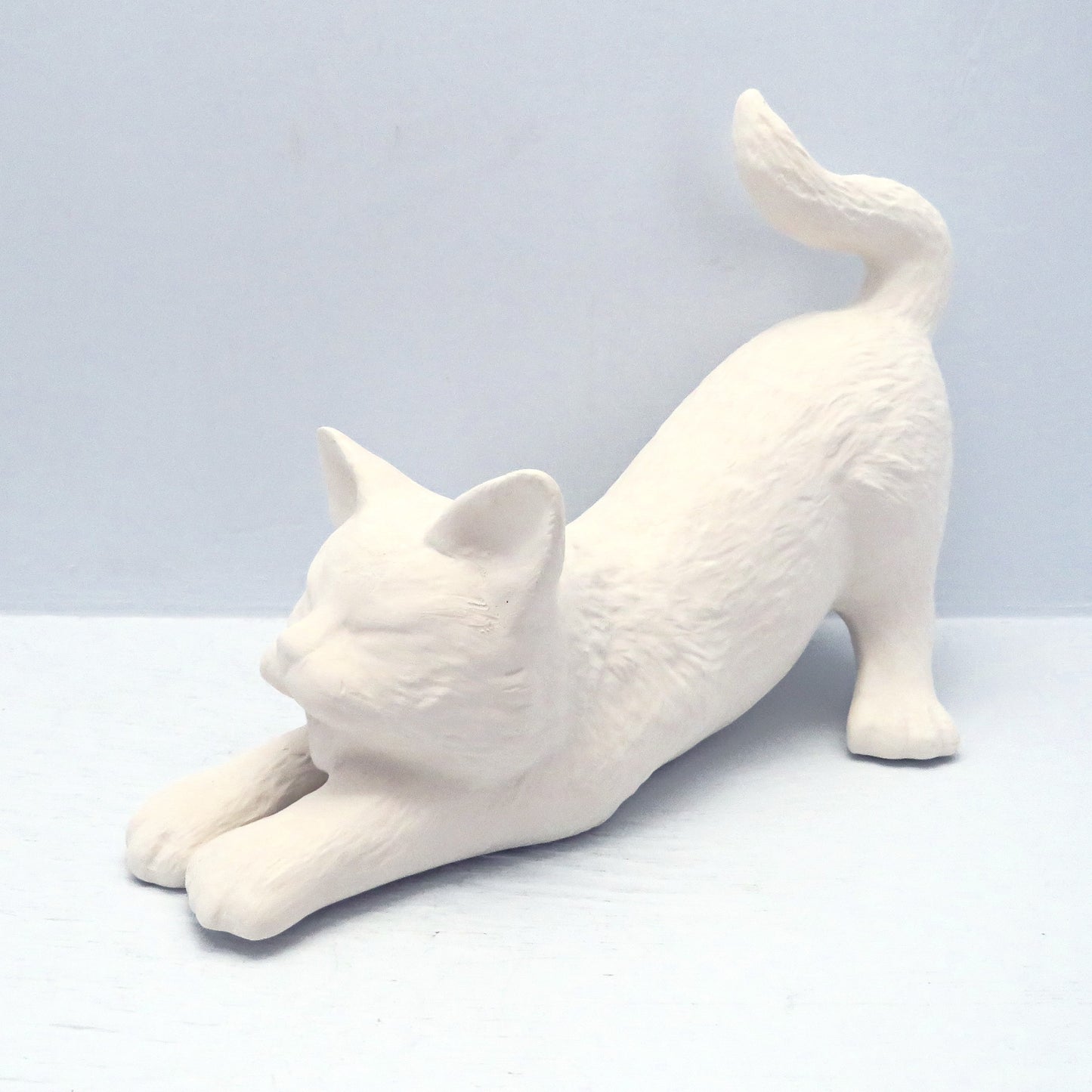 Handmade paint it yourself stretching cat angled with its head to the left on a pale blue background.
