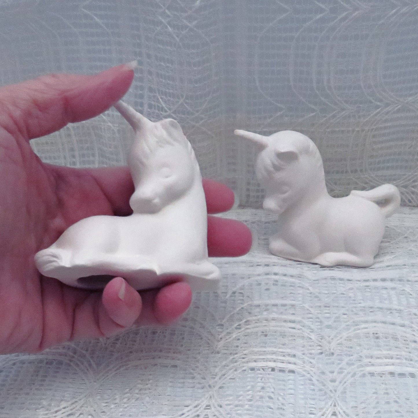 2 unpainted ceramic bisque unicorns with one in my hand for size comparison