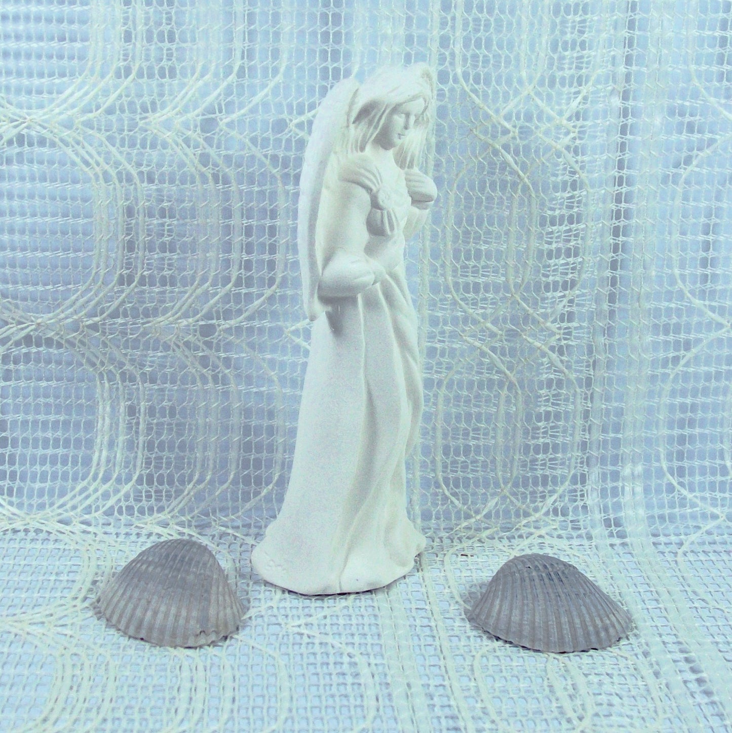 Side view of standing angel with wings tucked in.  She is standing on an ecru lacy table cloth.