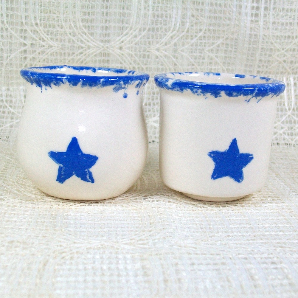 1 set of 2 white glossy ceramic votive holders with blue trim around the top and blue stars
