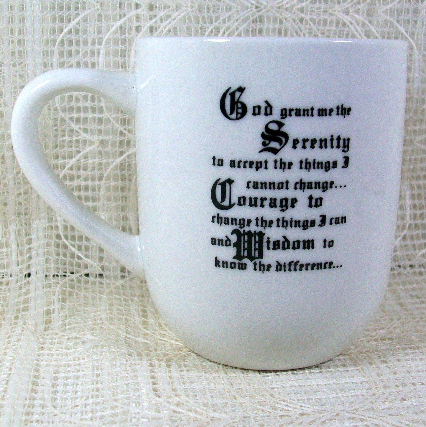 Close up of the white mug with the handle facing left and the Serenity Prayer on this side written in an Old English type black print