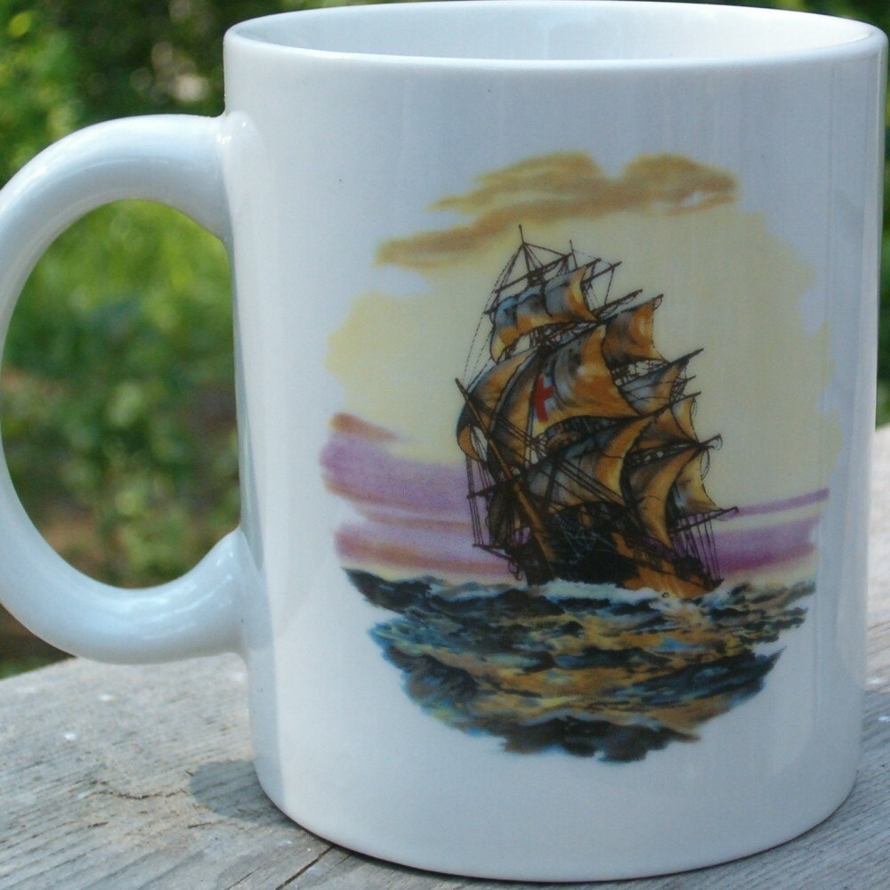 Back side of a white ceramic mug with clipper ship on this side, sailing on the ocean and a sunset sky.