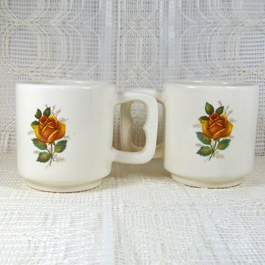 Handmade glossy glazed white ceramic mugs with the handles in, showing yellow roses on the sides of the mugs.