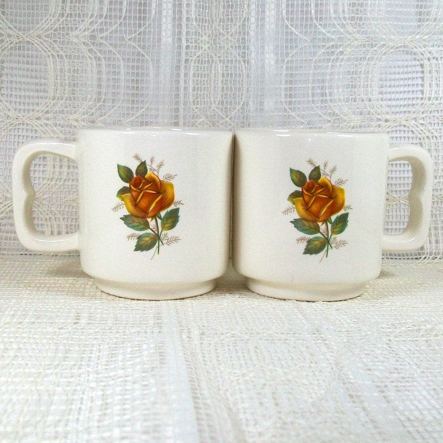 Set of 2 handmade white glossy 8 ounce mugs with a yellow rose on each side of the mug sitting on a lacy light colored background