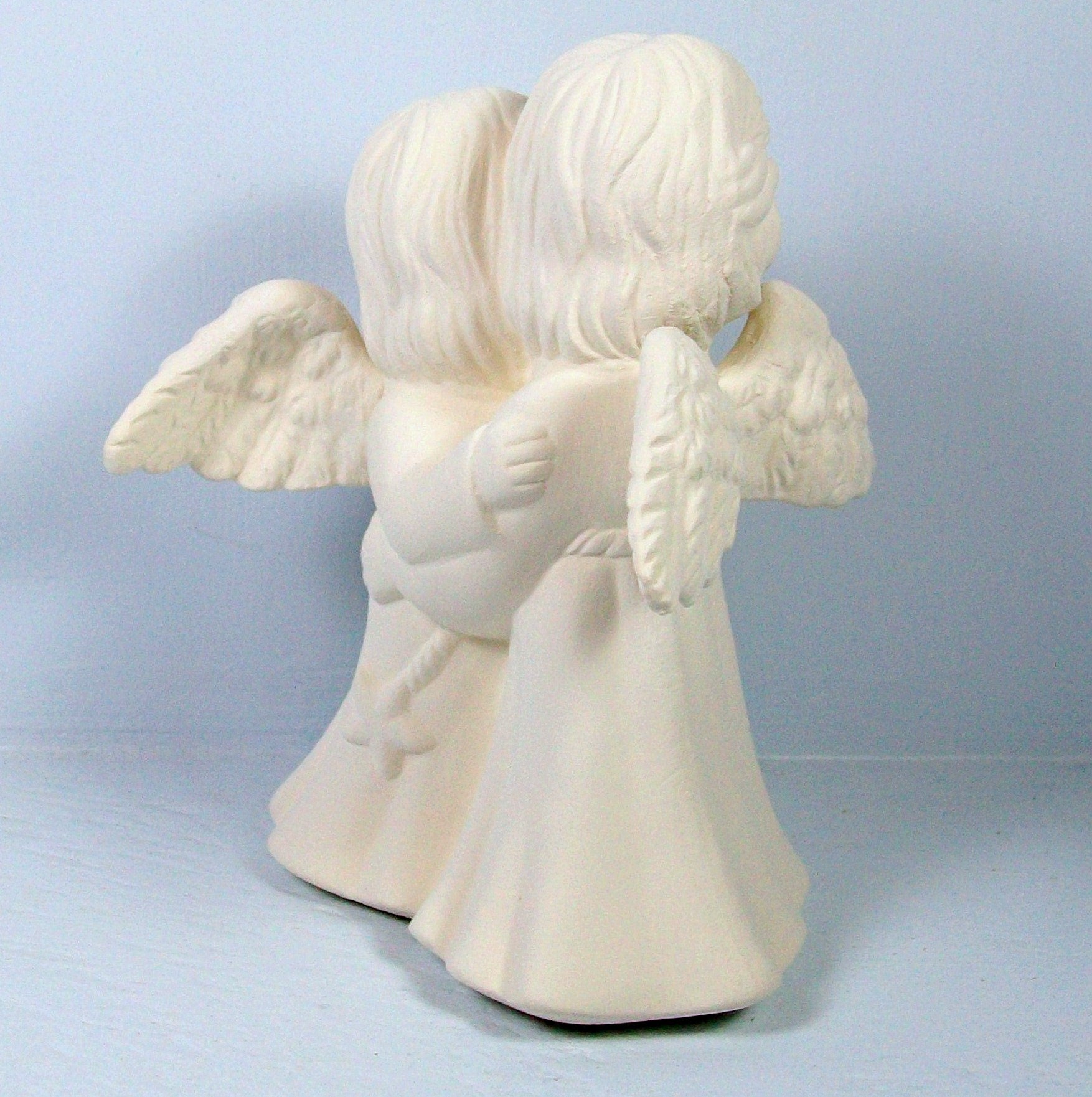 back view of taller angel in ready to paint ceramic hugging angel statues on a blue background