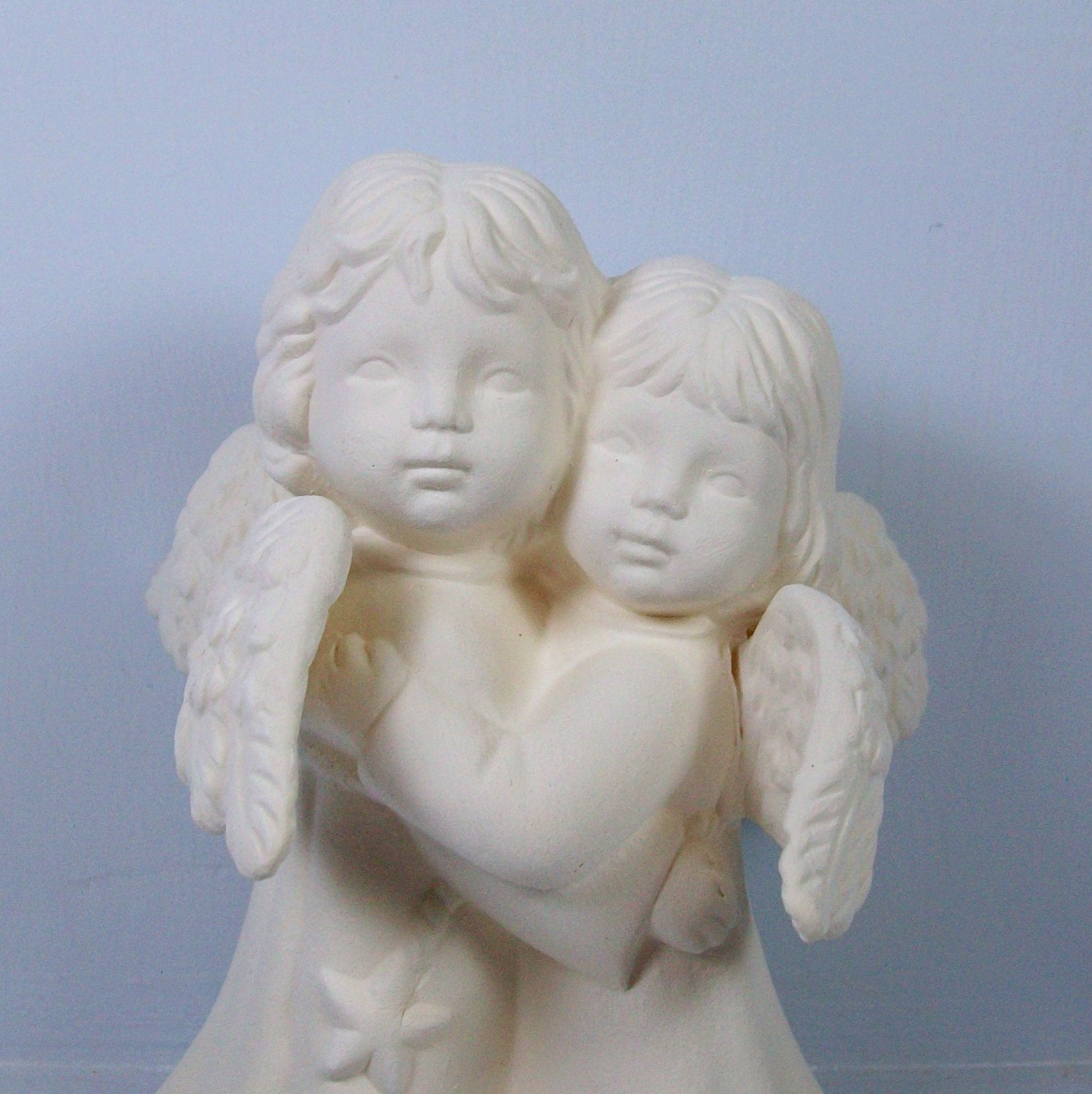 Close up showing faces of unpainted ceramic hugging angel statue