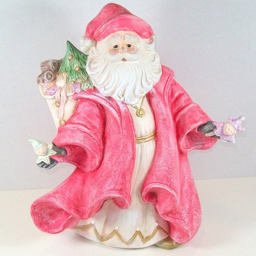 Handcrafted Ceramic Santa with toys in his hands and a bag of presents on his back.  He is wearing a beige tunic with gold trim and a red coat and hat.