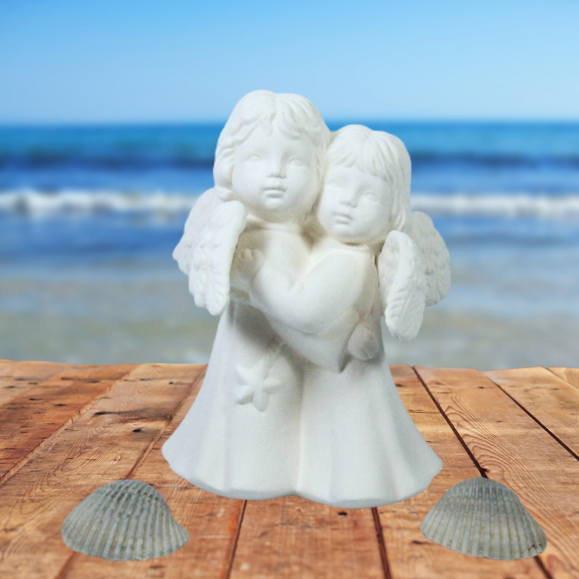 Ready to Paint Ceramic Hugging angels figurine on a table by the ocean with sea shells near