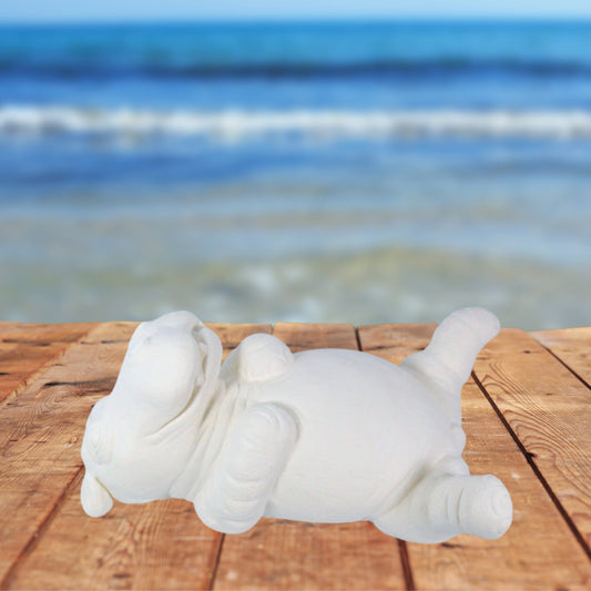 ready to paint ceramic hippo figurine on his back  on a wood table by the ocean.